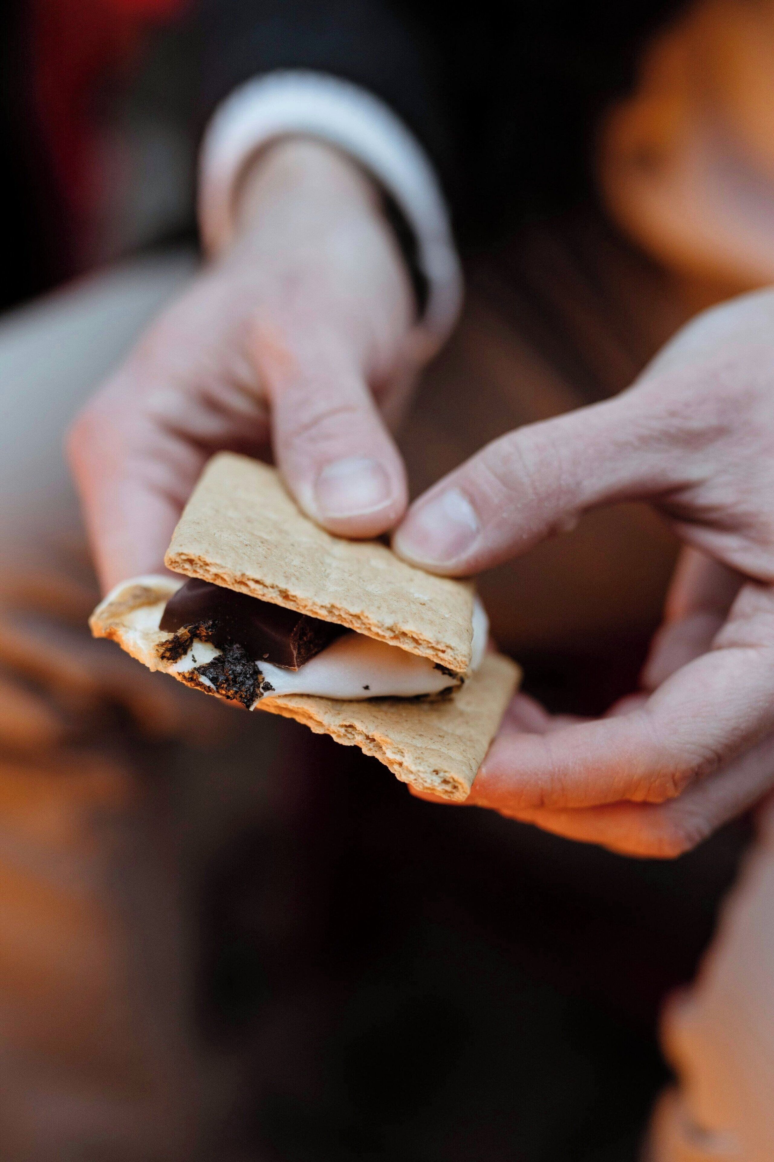 A person holding a sandwich with two pieces of bread, a filling, and a chocolate piece.
