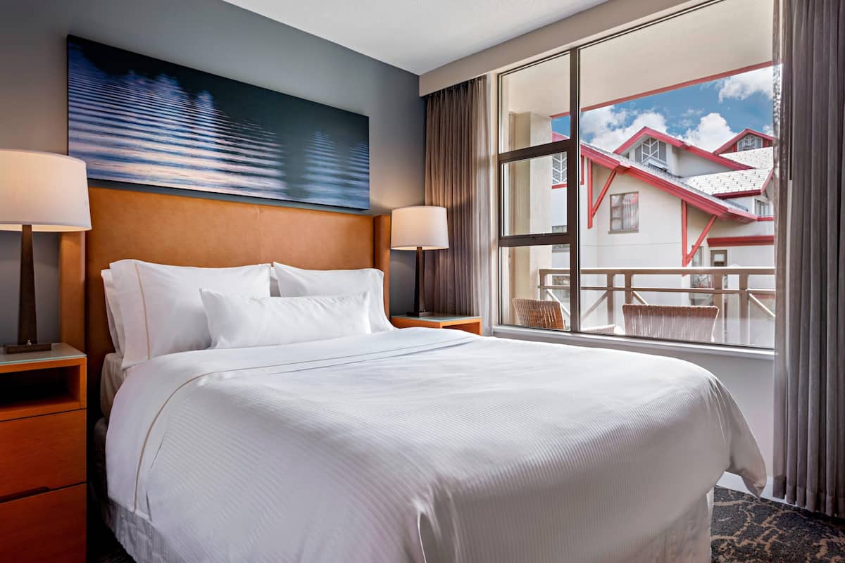 A hotel room with a large bed, two bedside tables, a window with a view of buildings, and a painting on the wall.