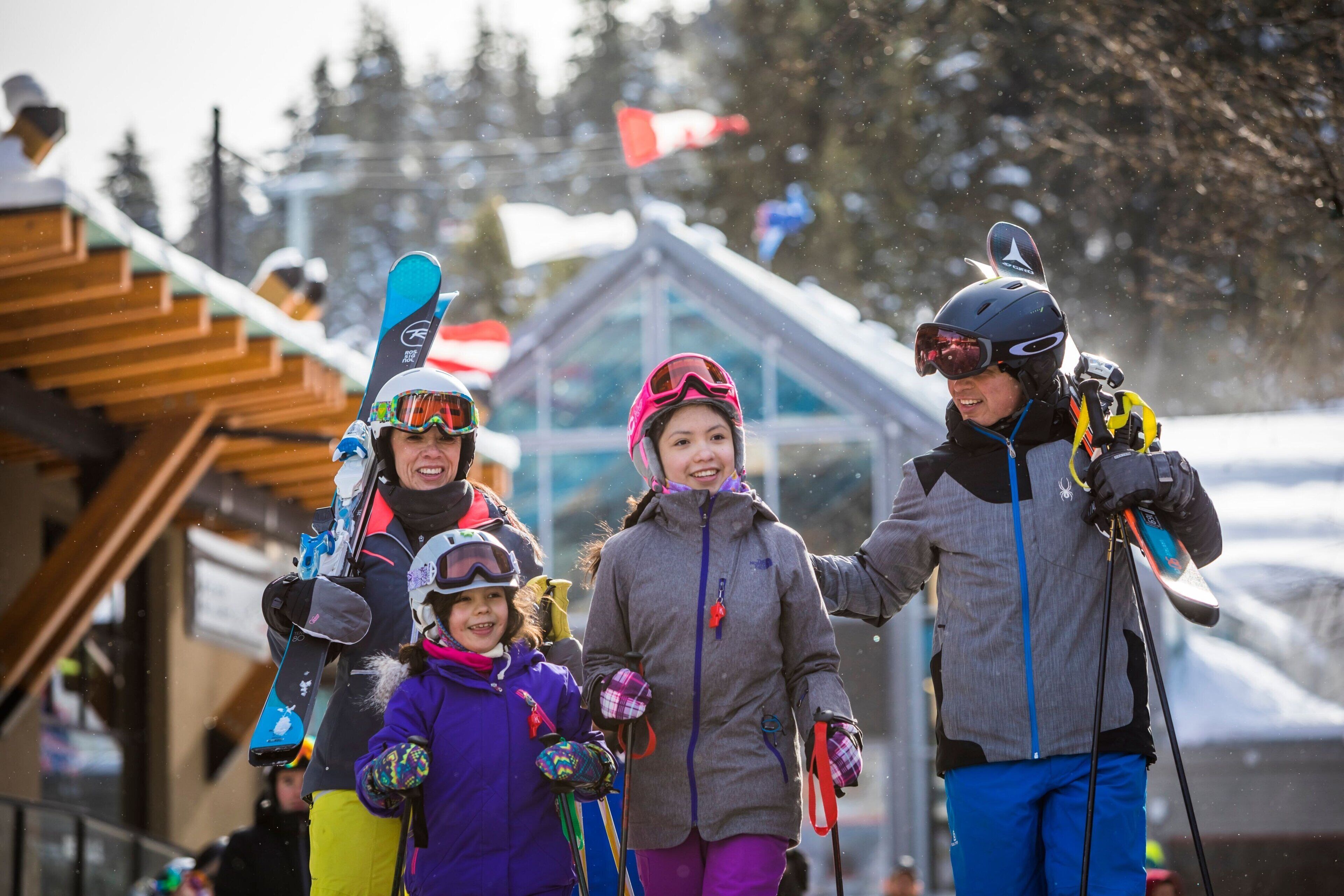 Un grupo de personas con esquíes y tablas de snowboard caminando hacia un edificio con techo inclinado.