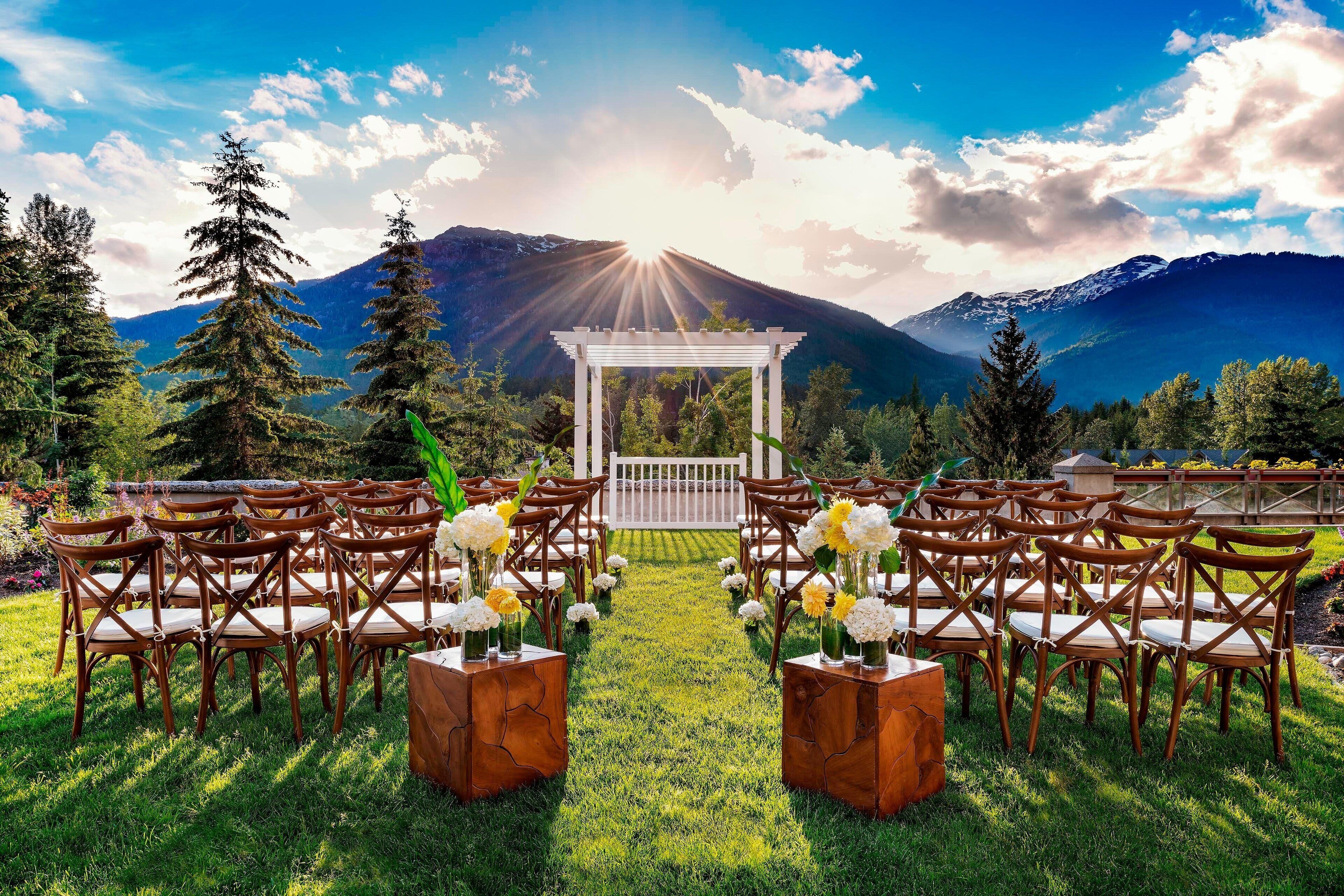 Une cérémonie de mariage avec une arche blanche et des chaises disposées en rangées, le tout installé devant un paysage montagneux.