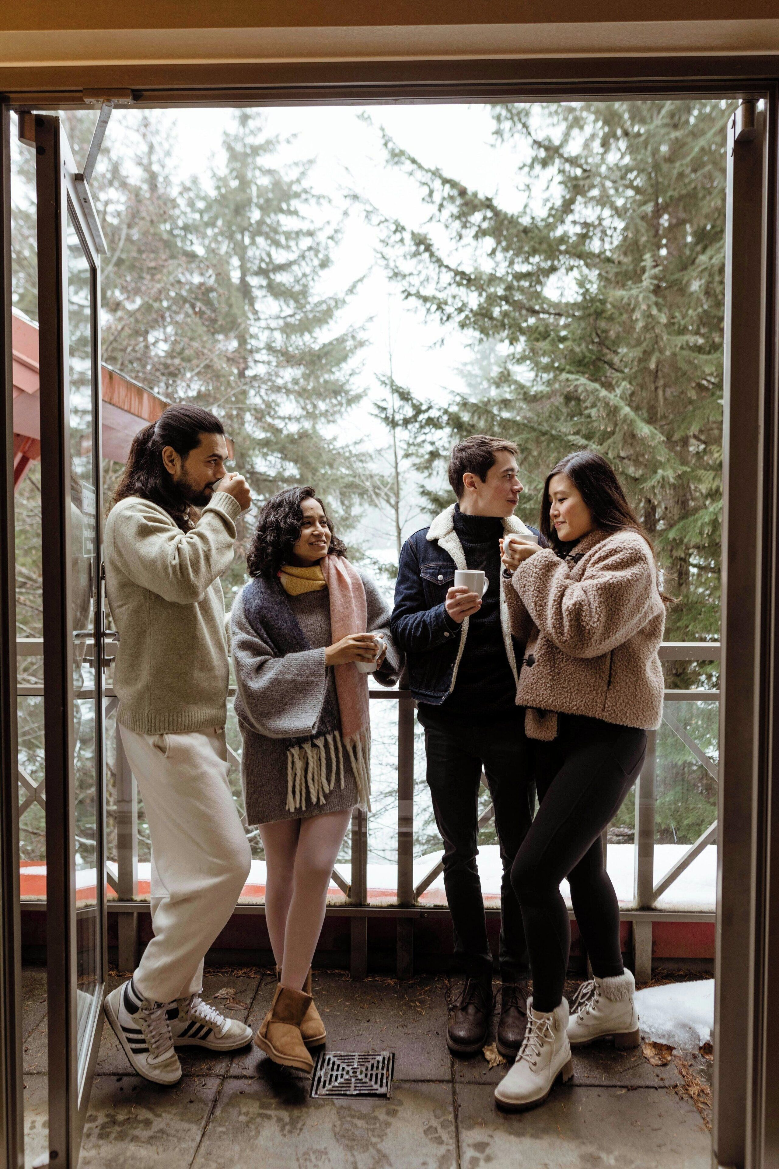 A group of people standing indoors near a glass door, with a view of trees outside.