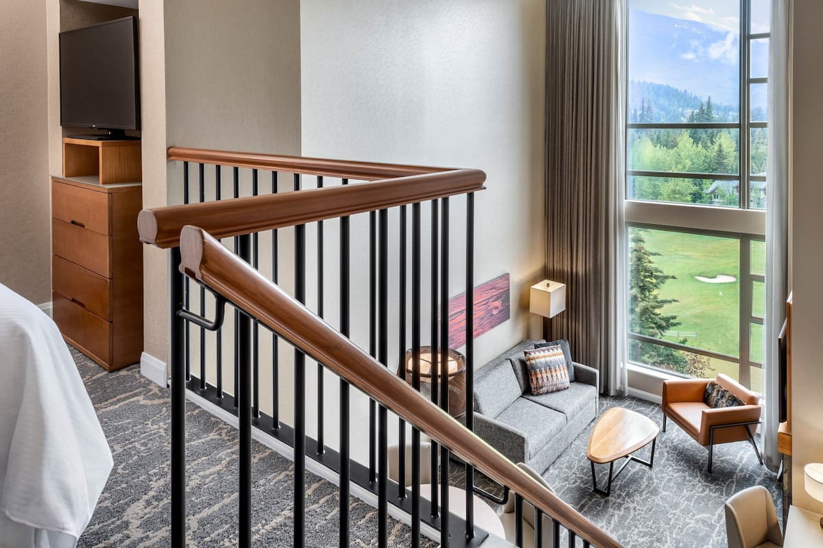 A hotel room with a wooden staircase, a sofa, a coffee table, and a view of a golf course.