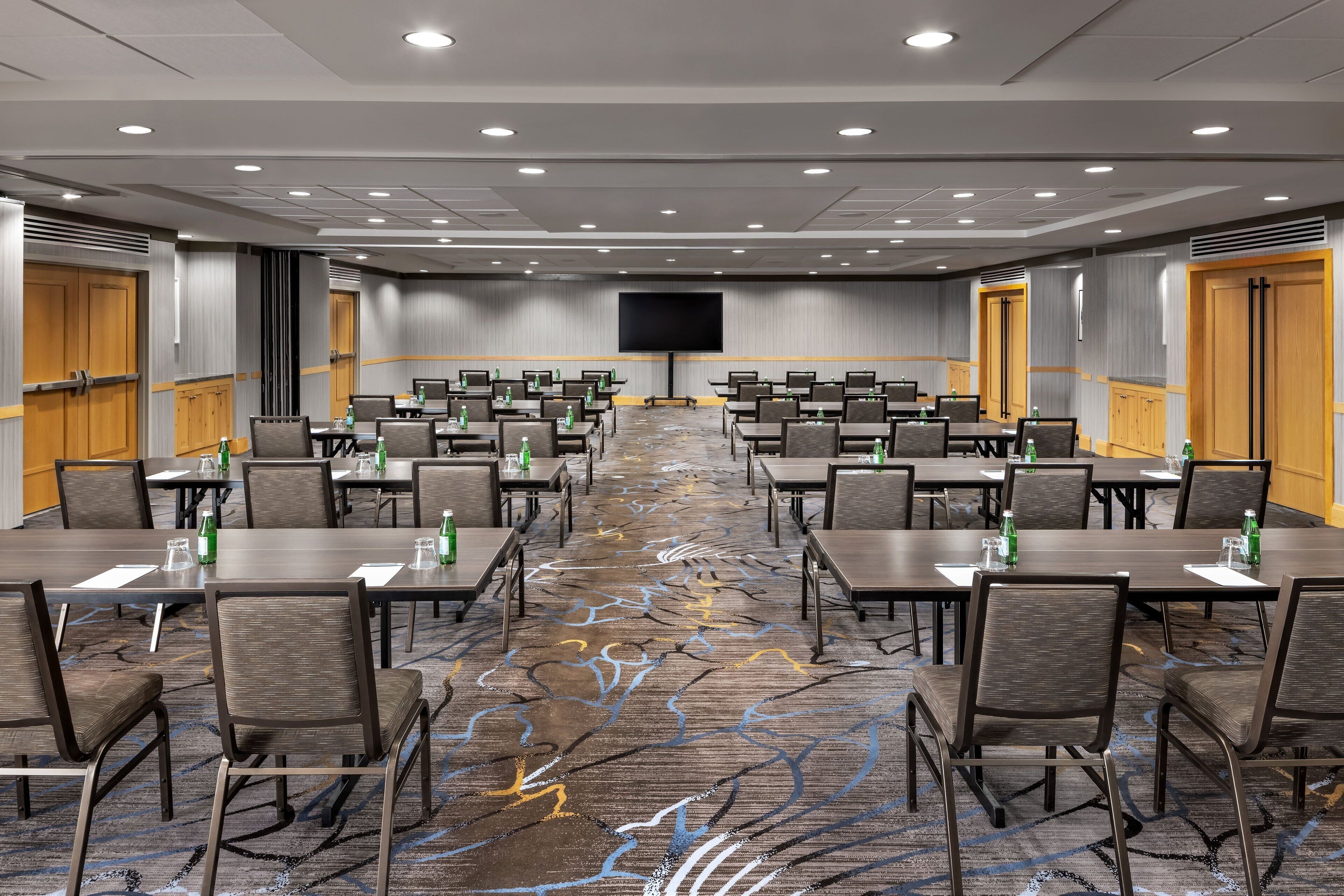 A conference room with rows of tables and chairs, a large screen, and a patterned carpet.