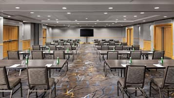 A conference room with rows of tables and chairs, a large screen, and a patterned carpet.