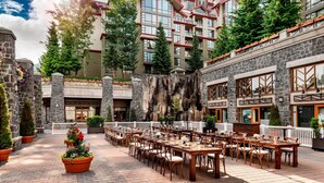 Un patio con mesas y sillas para comer al aire libre, paredes de piedra y un edificio grande con varios pisos y balcones.