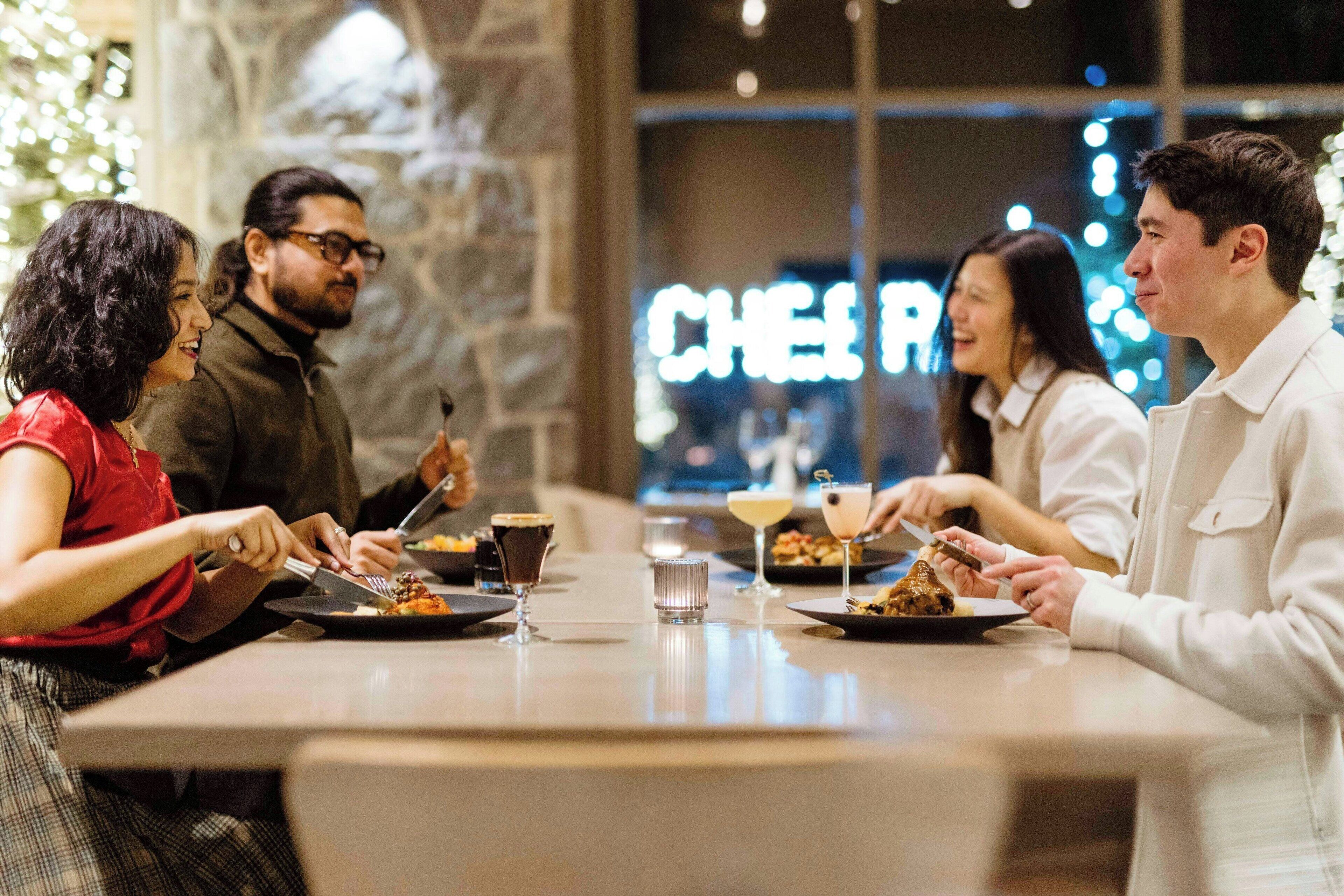 Un grupo de personas cenando en un restaurante con una pared de piedra y un letrero de neón al fondo.