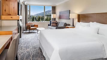 Quarto de hotel com uma cama grande, uma escrivaninha, uma cadeira, um sofá e uma televisão fixada num painel de madeira.