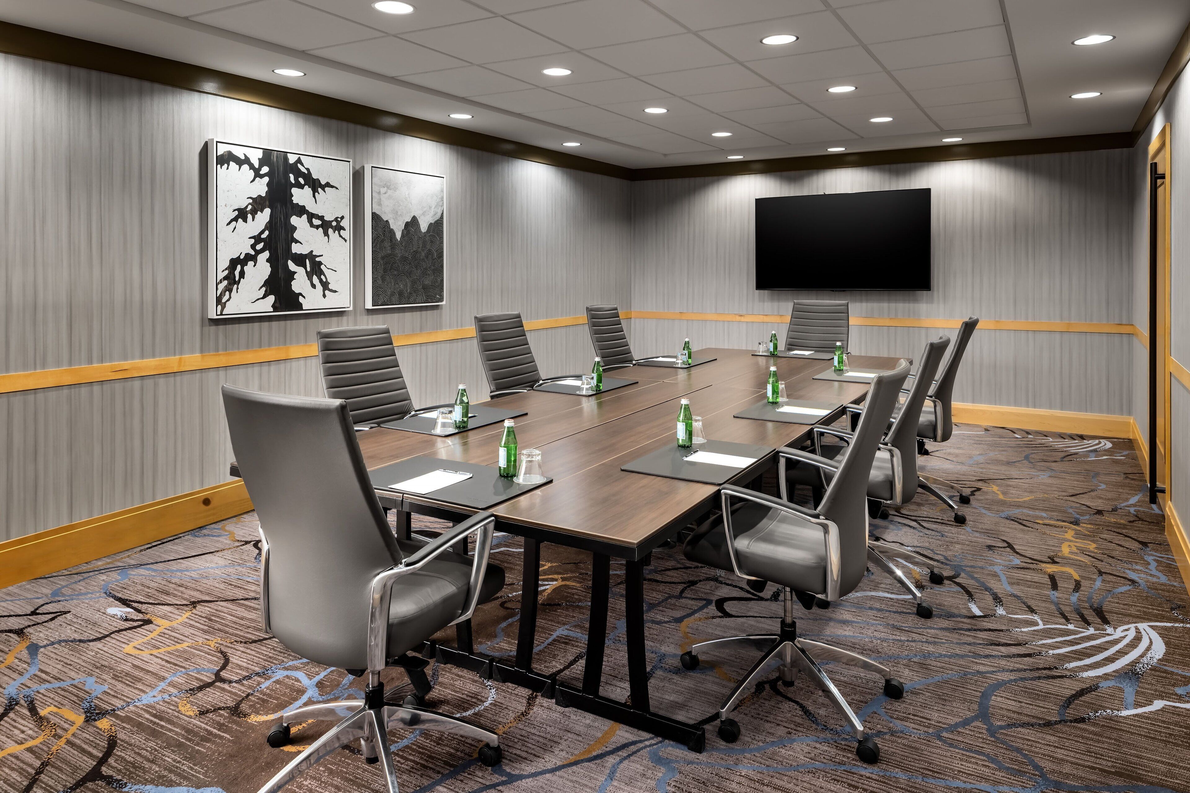 A conference room with a long table, multiple chairs, water bottles, and a flat-screen TV on the wall.