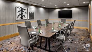 A conference room with a long table, multiple chairs, water bottles, and a flat-screen TV on the wall.
