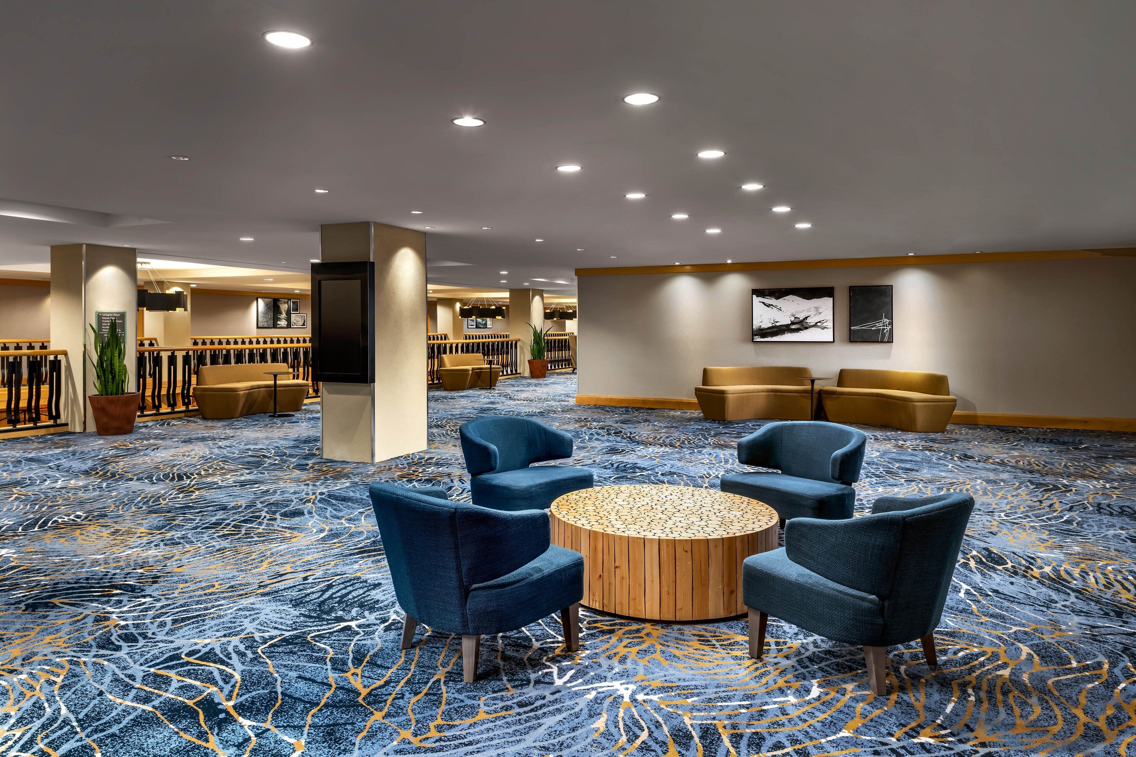 A hotel lobby with a blue patterned carpet, round wooden coffee table, and blue armchairs.