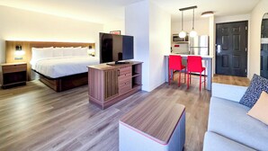 Habitación de hotel con cama, televisor, kitchenette pequeña, zona de comedor con sillas rojas y un sofá.