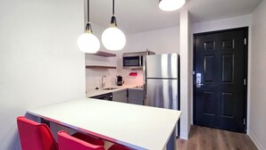 Una cocina moderna con encimera blanca, sillas rojas, electrodomésticos de acero inoxidable e iluminación colgante.
