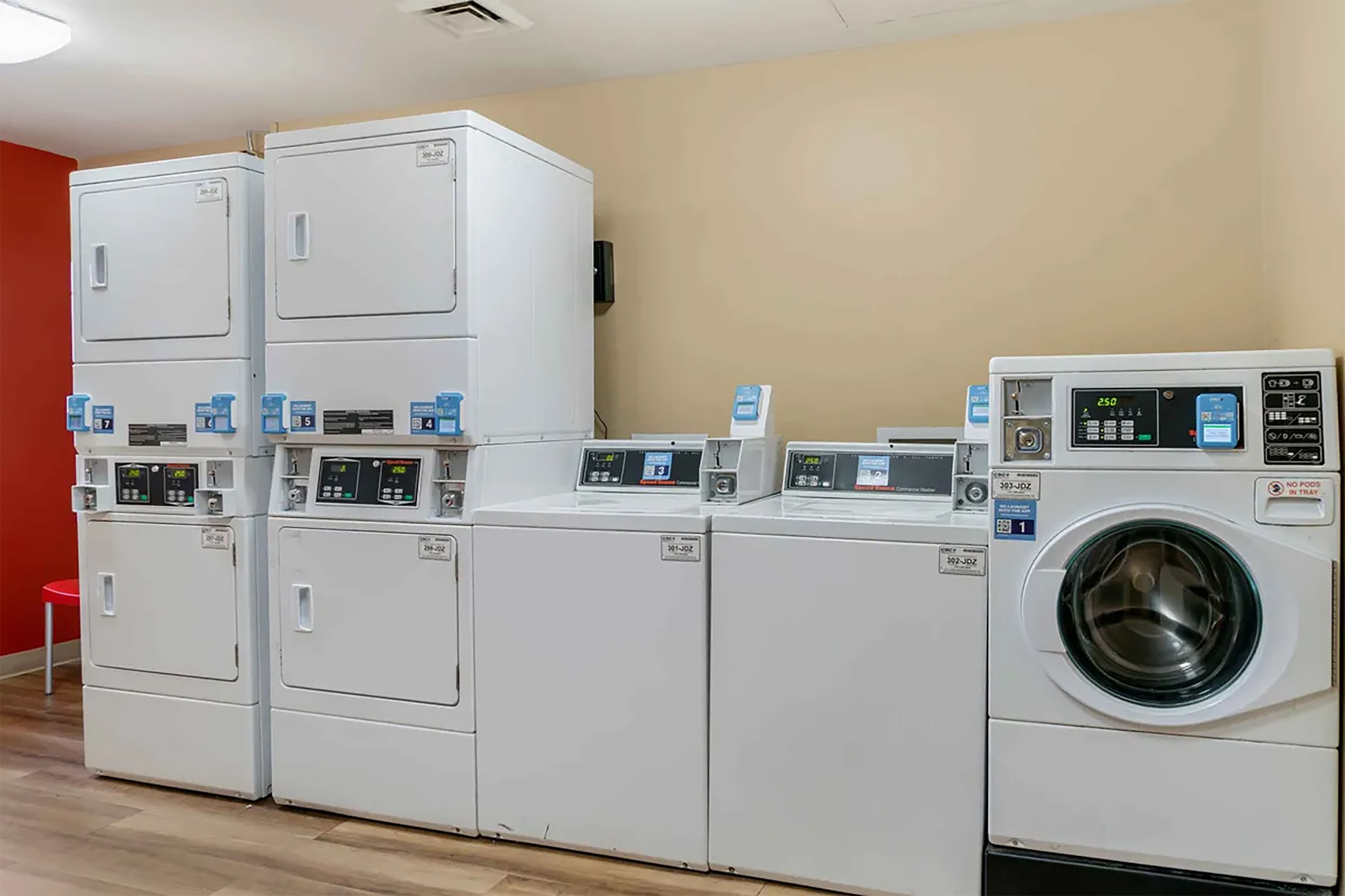 A laundry facility with multiple washing machines and dryers, a red chair, and a beige wall.