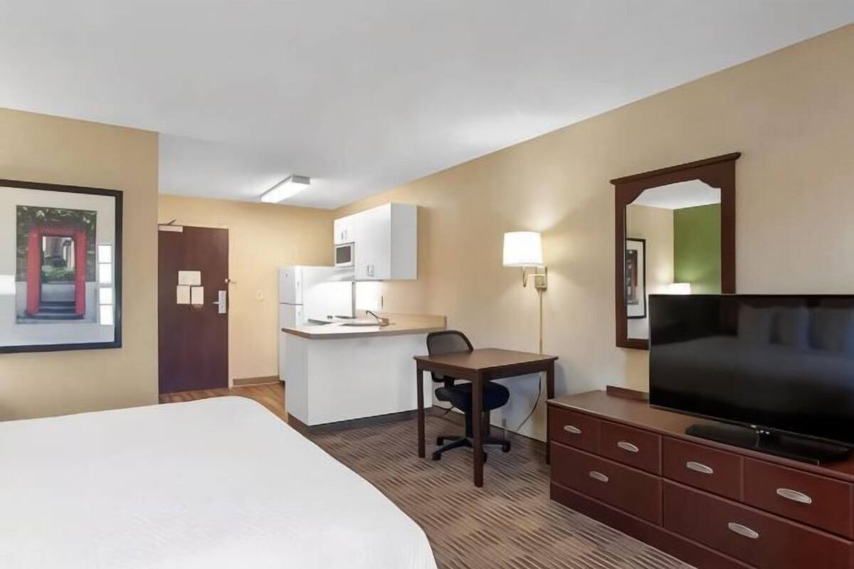 Ein Hotelzimmer mit Bett, Schreibtisch, Fernseher, Spiegel und einer Küchenzeile.