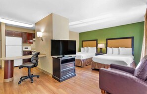 Habitación de hotel con kitchenette, televisión, cama con dos almohadas, escritorio con silla y sofá.