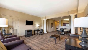 A hotel room with a living area, a dining table, and a TV mounted on the wall. - Extended Stay America Suites Houston Med Ctr Braeswood Bl (Houston)