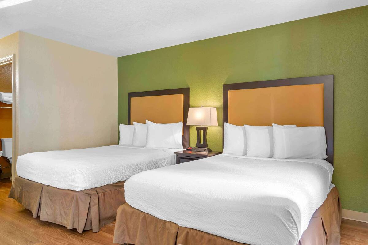 Habitació d'hotel amb dos llits, una tauleta de nit amb una làmpada i una paret d'accent verd.