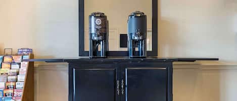 A black cabinet with two coffee makers on top, a mirror above, and a row of books on the left.