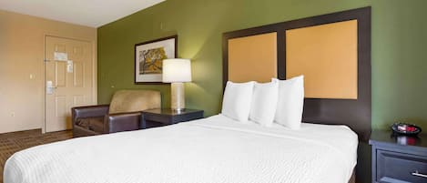 Habitación de hotel con una cama grande, una silla, una mesita de noche con lámpara y una obra de arte colgada en la pared.