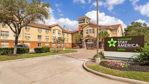 Un hôtel Stay America proposant des suites et des services prolongés, avec une entrée bien visible, un panneau indicateur et un jardin bien entretenu.