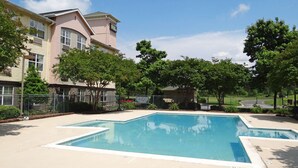 Une piscine entourée d’une clôture, avec des arbres et un bâtiment portant une enseigne.