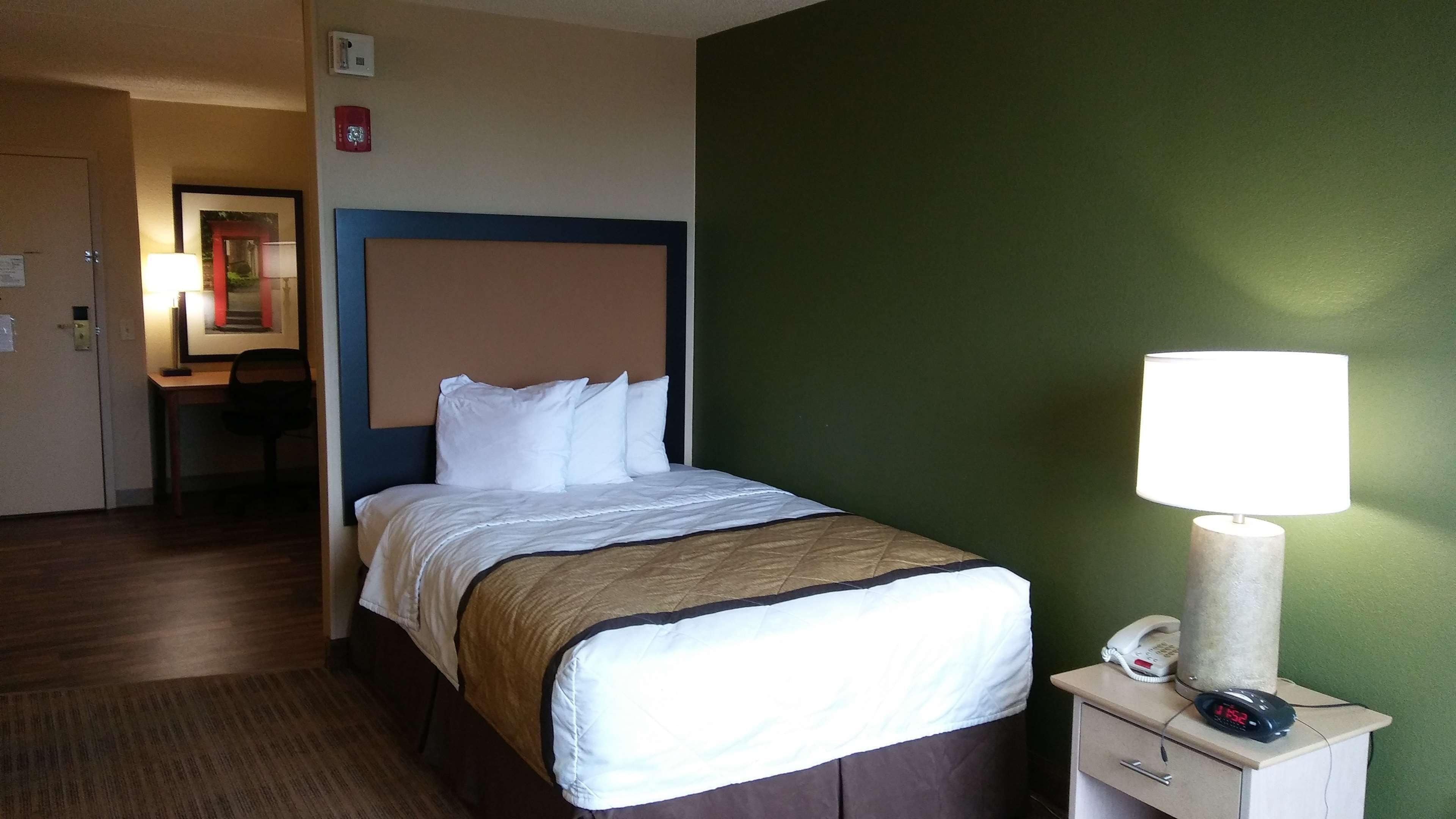A hotel room with a bed, bedside table with a lamp, and a desk.