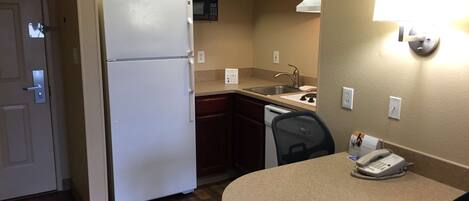 A compact kitchen with a refrigerator, microwave, sink, and a small dining table with a chair.