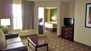 Une chambre d’hôtel avec un canapé, une petite table, un téléviseur posé sur une commode et un lit à l’arrière-plan.