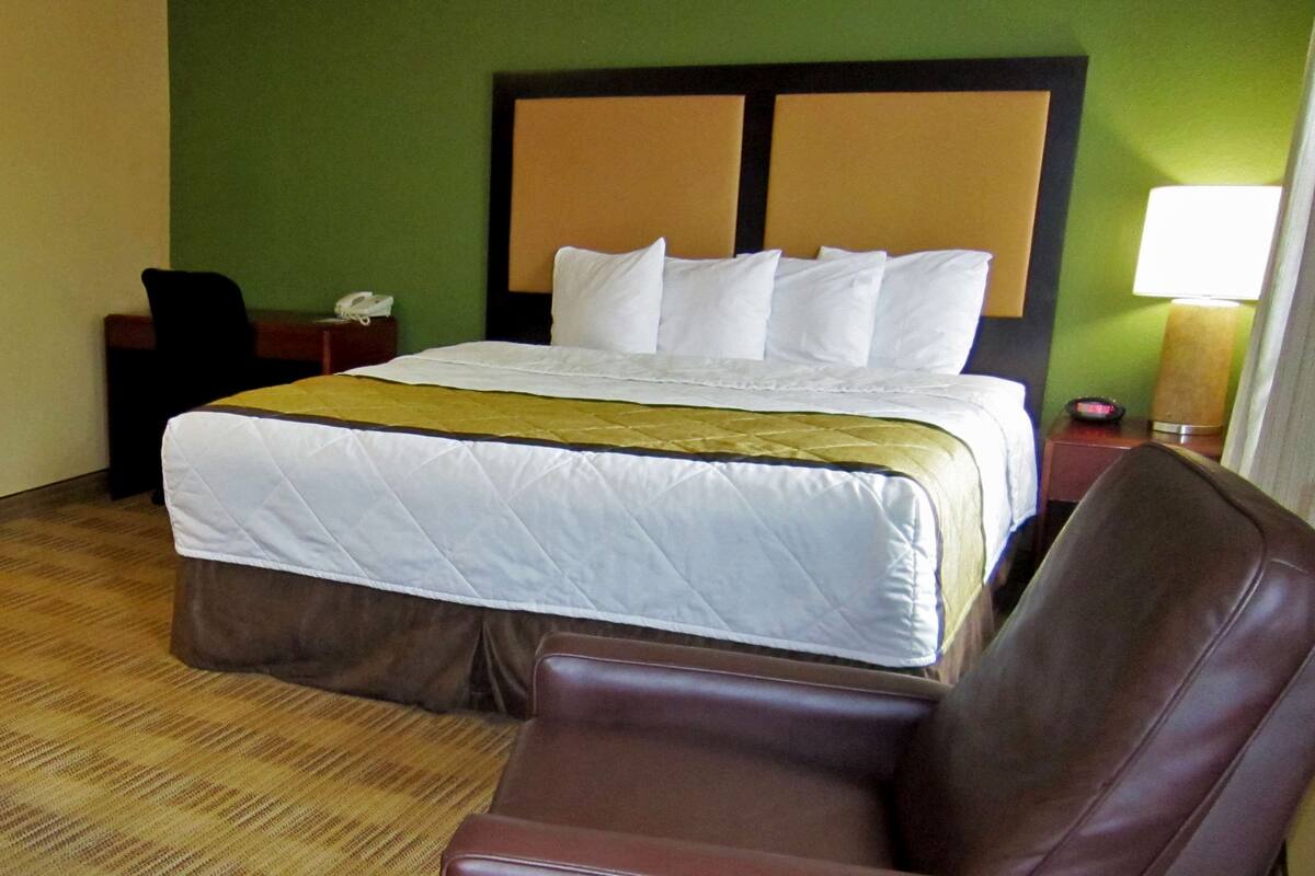 Een hotelkamer met een bed, een bruine leren fauteuil, een nachtkastje en een lamp.