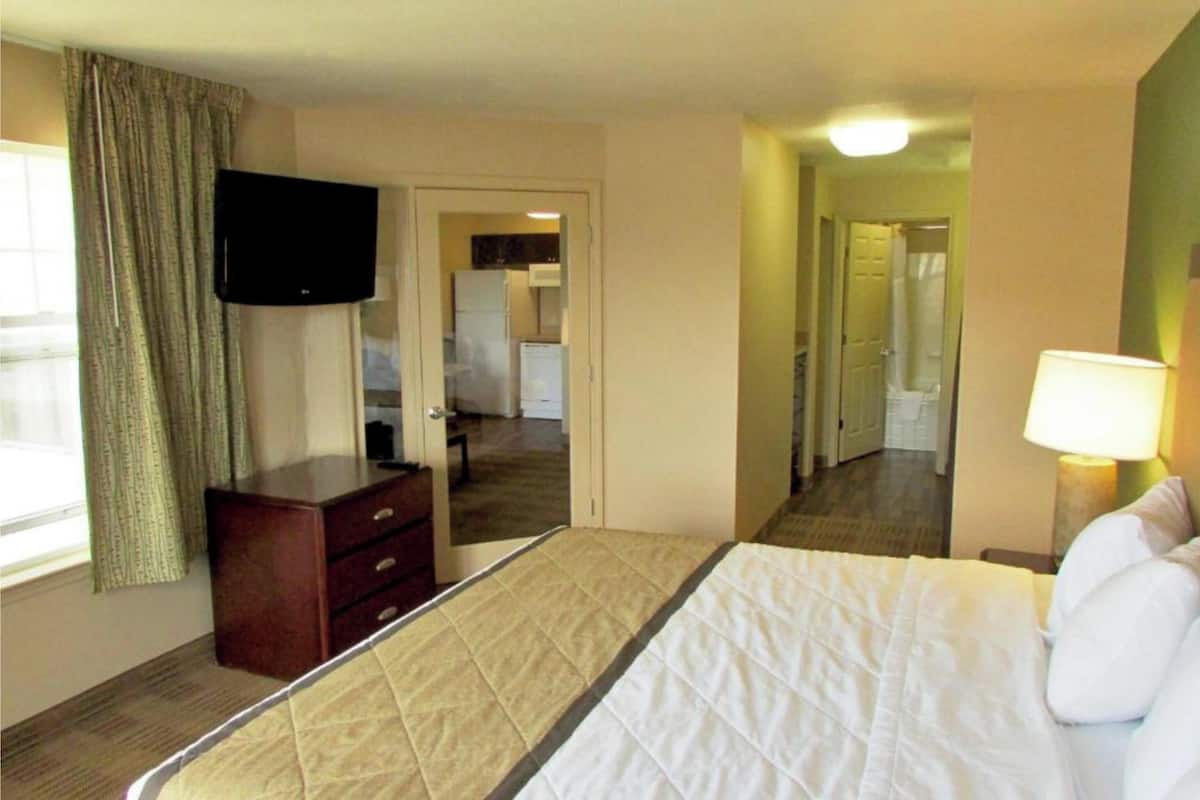 A hotel room with a bed, a dresser, a television, and a lamp.