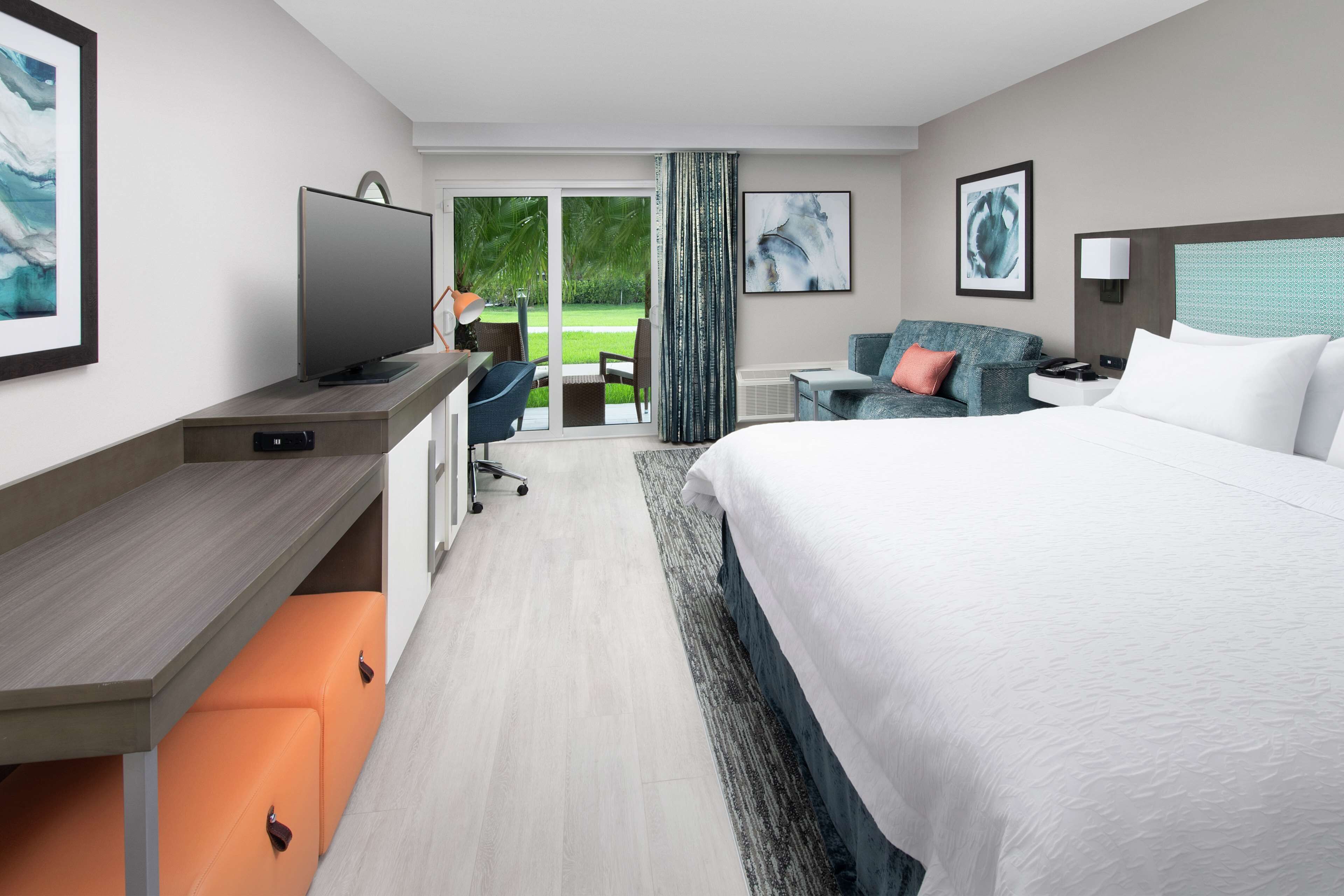 A modern hotel room with a large bed, a desk with a computer, a television, and a view of the outdoors.