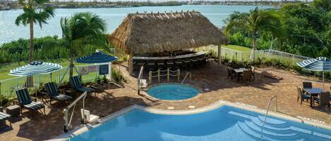 A pool area with lounge chairs, a thatched-roof structure, and a view of the ocean.