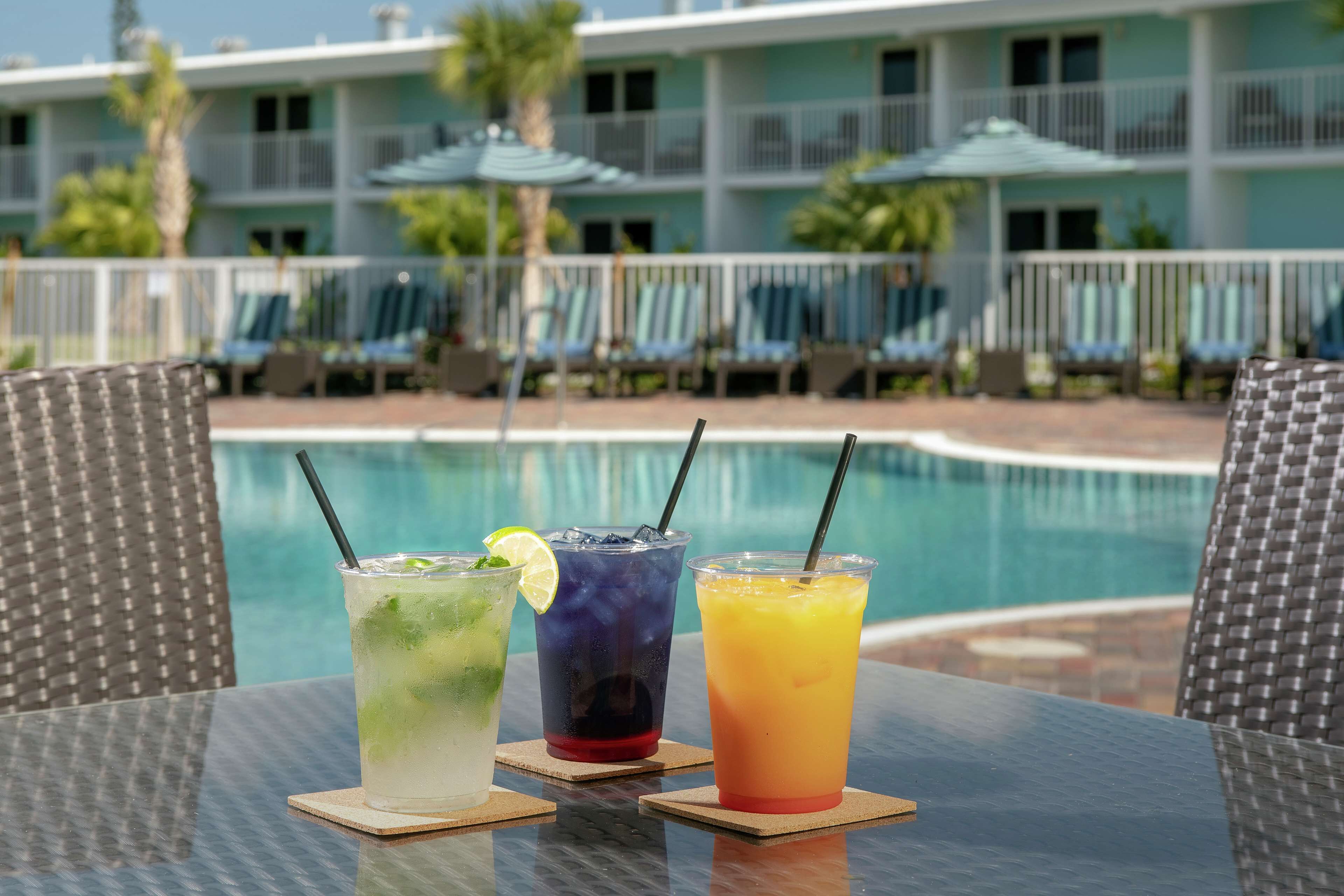 A table with three drinks in front of a pool, with a hotel building in the background.