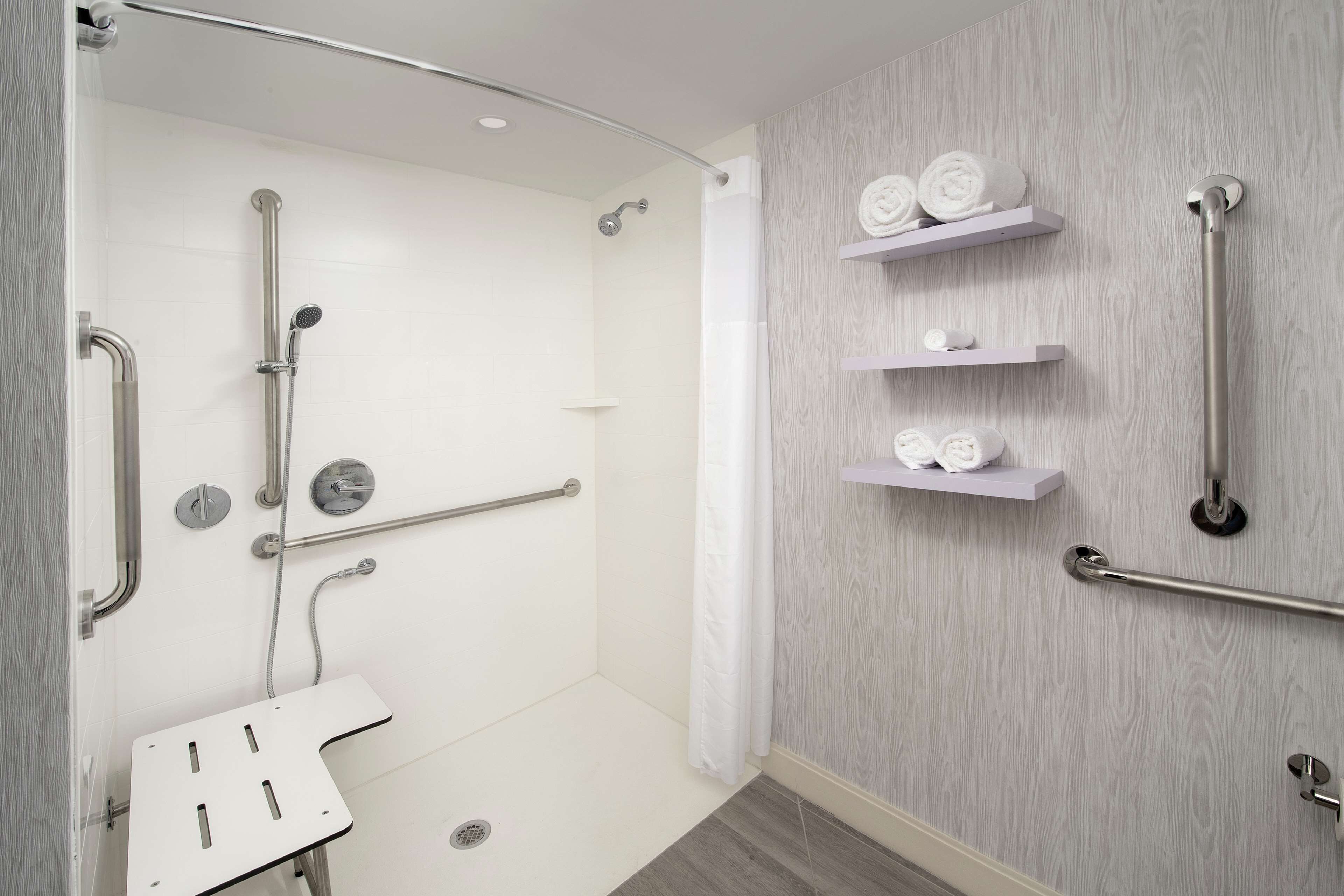 Ein modernes Badezimmer mit barrierefreier Dusche, Haltegriffen und einem weißen Waschbecken.