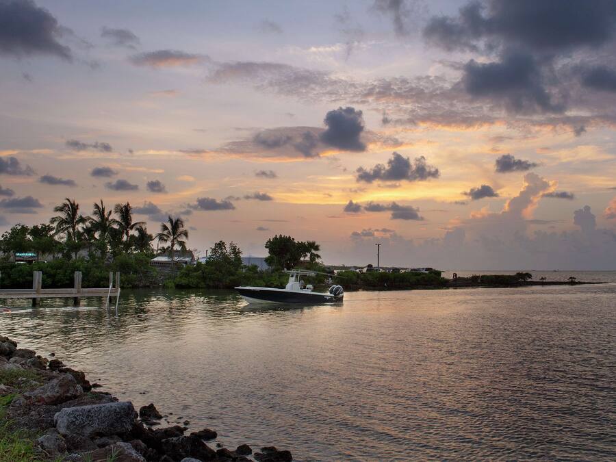 Un bote en aguas tranquilas cerca de un muelle, con un atardecer al fondo.