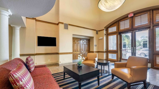 A lobby with a red sofa, a beige armchair, a black coffee table, and a TV mounted on the wall.