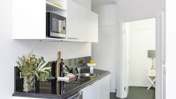 A modern kitchen with white cabinetry, a built-in microwave, and a black countertop. There is a vase with flowers on the counter, and a door leading to another room.
