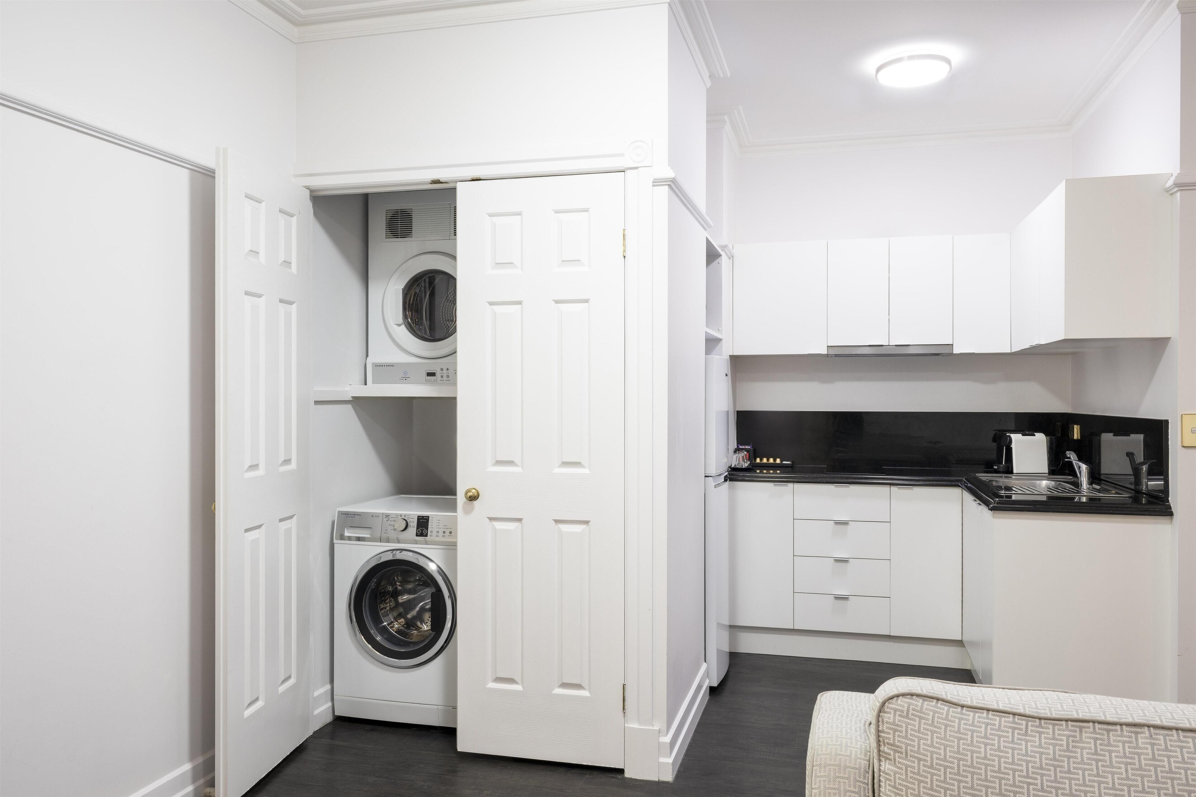 A compact laundry room with a washing machine and dryer, adjacent to a kitchenette with white cabinets and a black countertop.