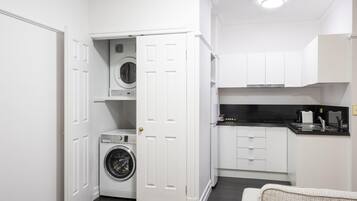 A compact laundry room with a washing machine and dryer, adjacent to a kitchenette with white cabinets and a black countertop.