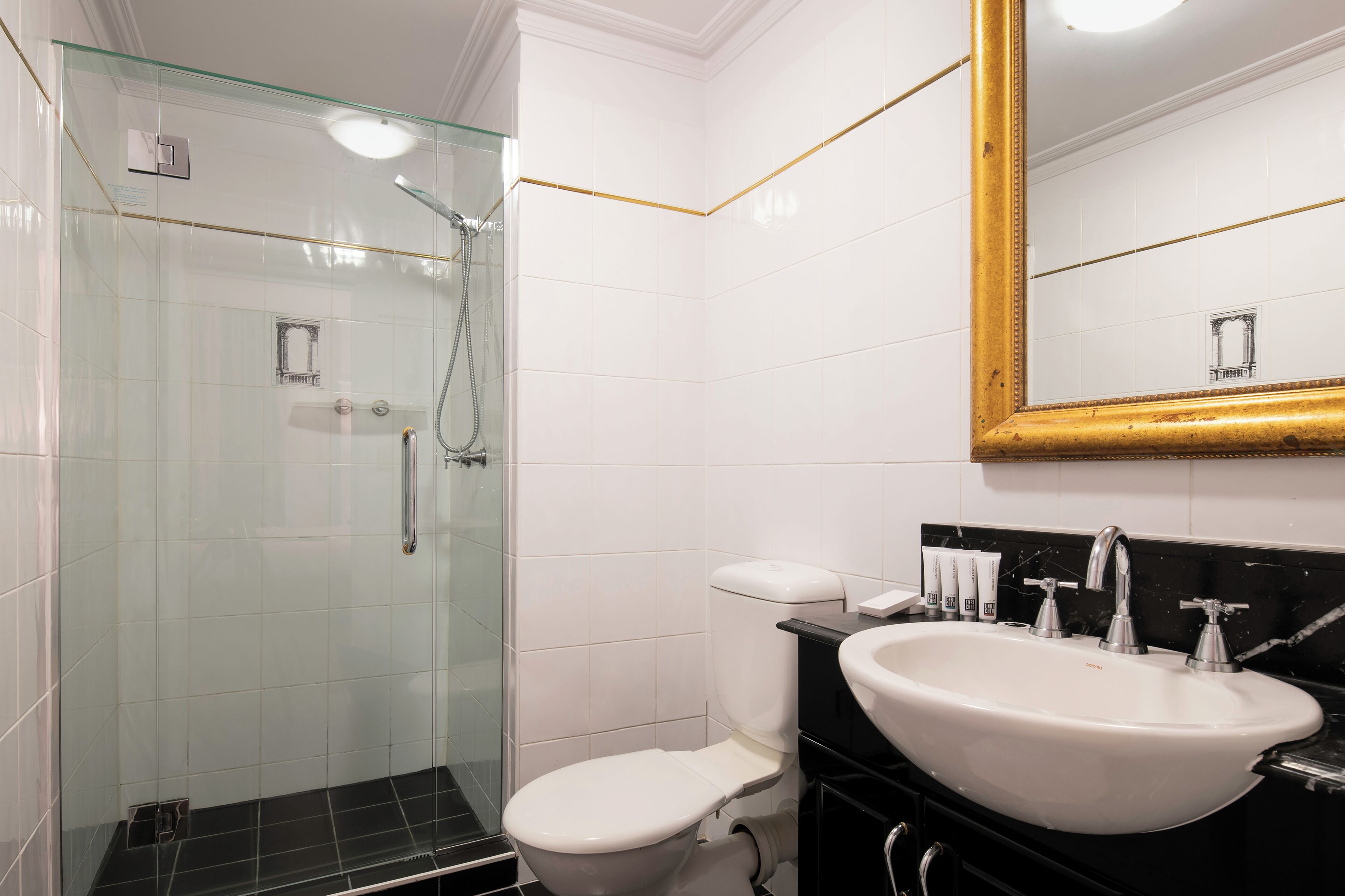 A bathroom with a glass-enclosed shower, a white toilet, and a large sink with a mirror above it.