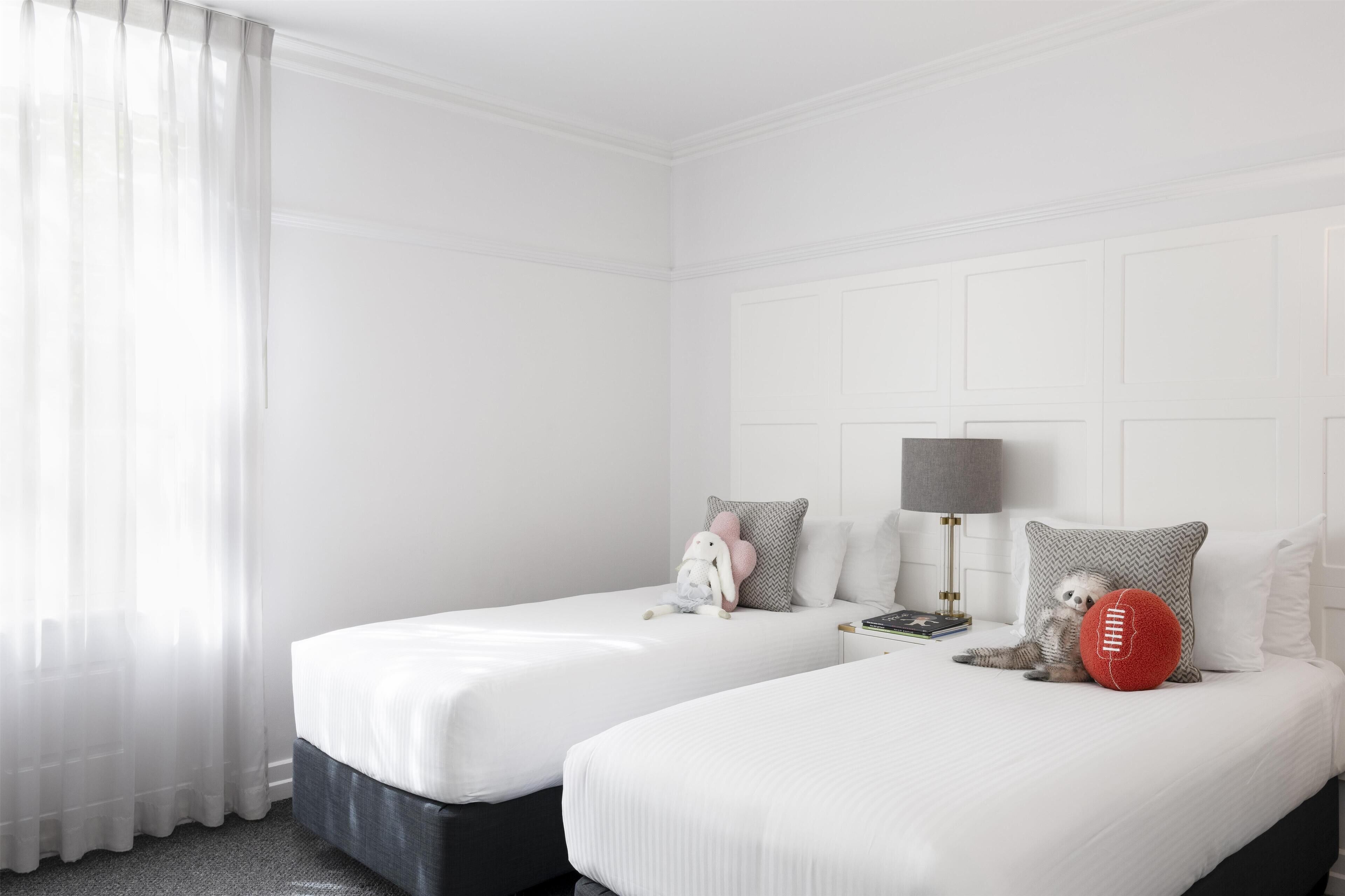 A hotel room with two beds, white bedding, a lamp, and a stuffed toy on one bed.