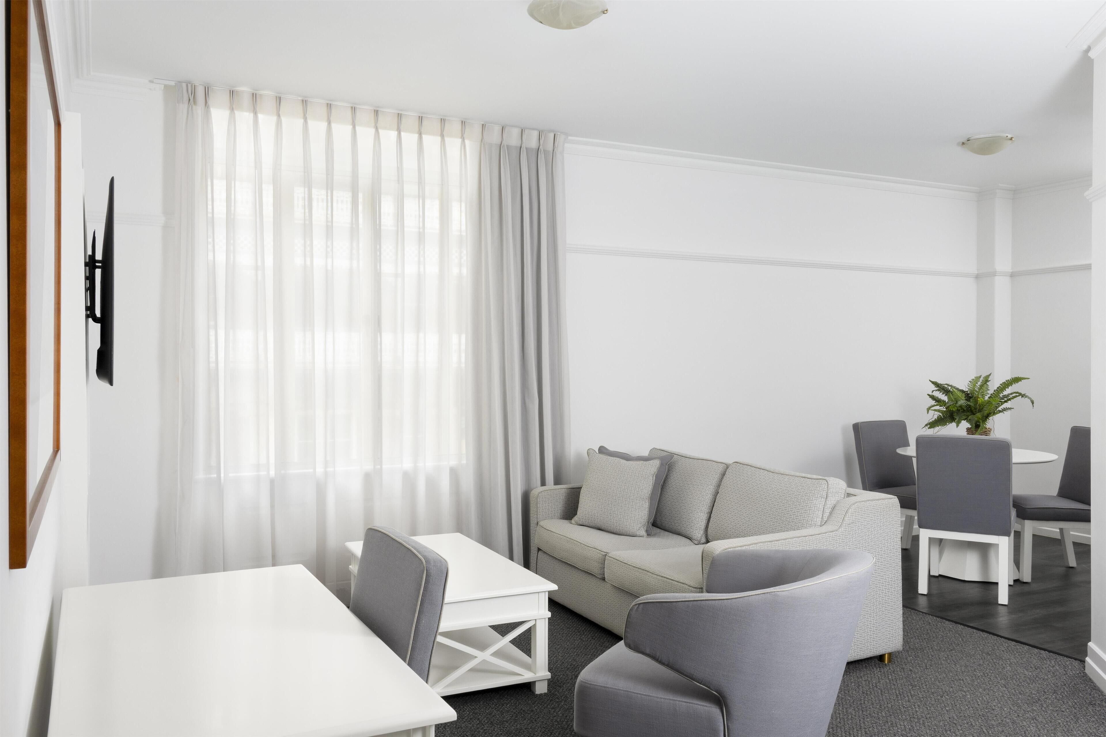 A modern, well-lit living room with a sofa, a dining table, and chairs.