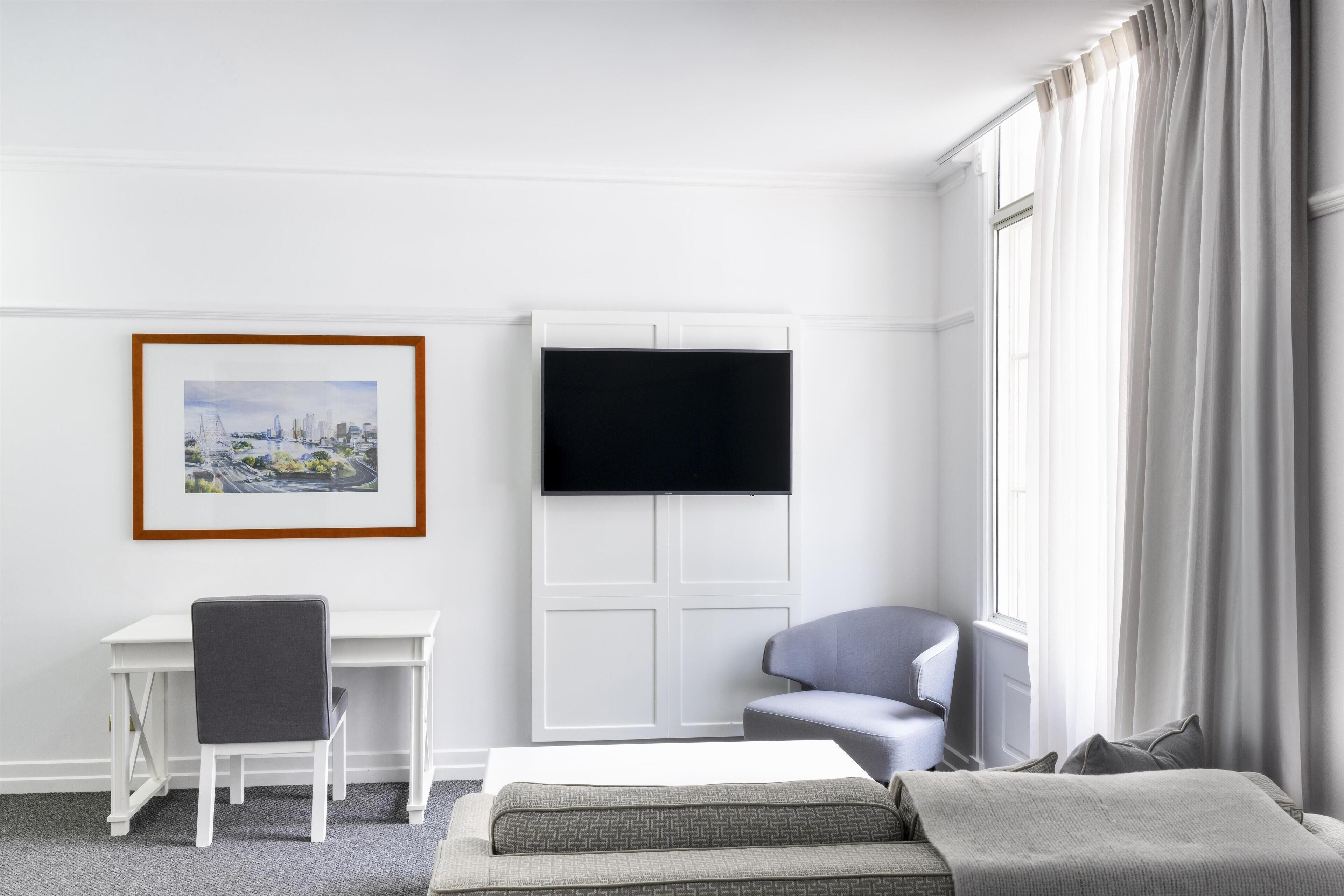 A hotel room with a bed, a desk, a chair, a TV, and a window with curtains.