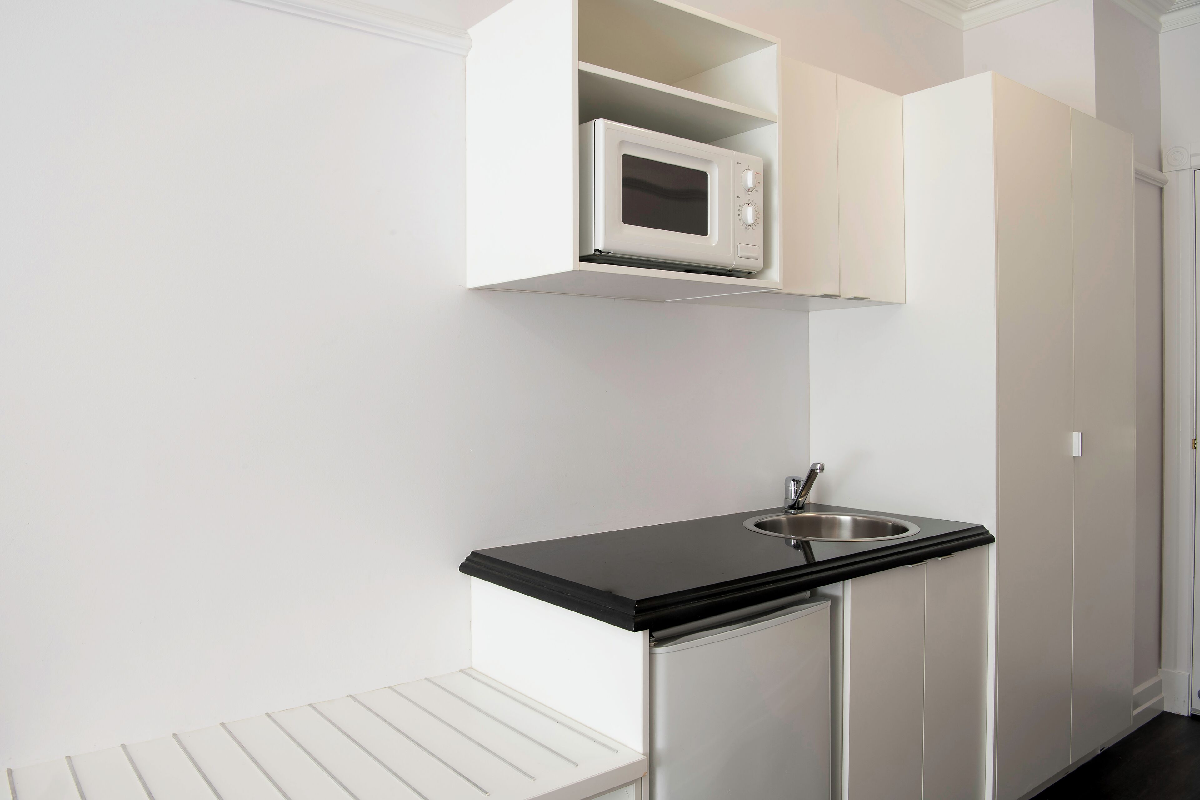 A compact kitchenette with a microwave, sink, and white cabinetry.