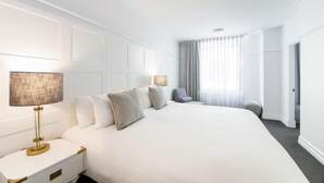 A hotel room with a large bed, bedside lamps, a chair, and a door leading to another room.