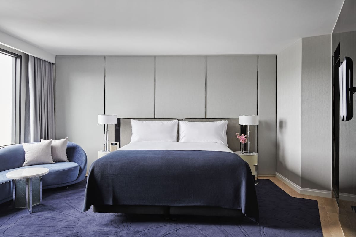 A modern hotel room with a large bed, a sofa, and a small table.