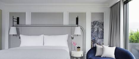 A modern hotel room with a large bed, a bedside table with a lamp, a small side table with a radio, and a blue sofa with pillows.