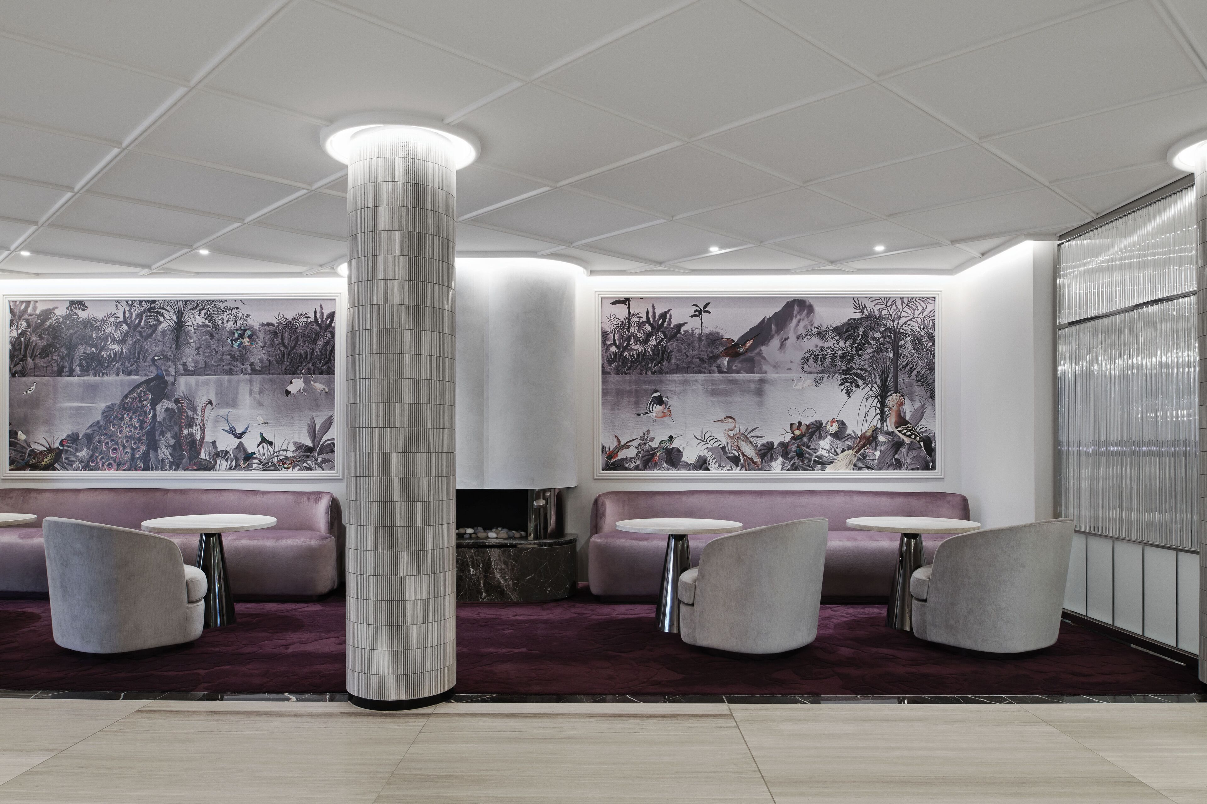 Un lobby moderno con una columna central, zonas de estar y grandes murales en las paredes.