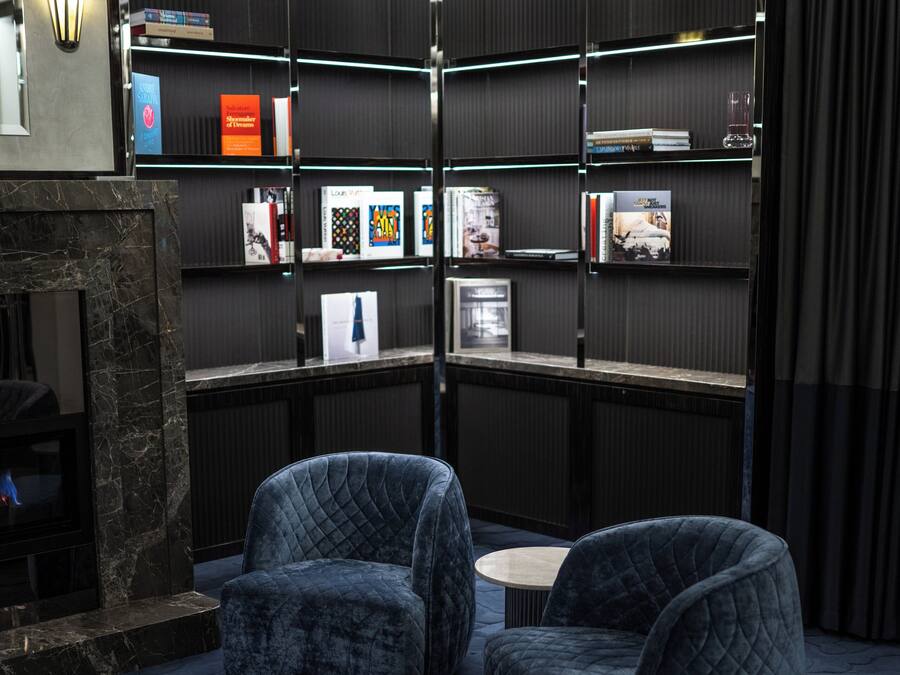 Un espacio de lectura moderno con dos sillones tapizados, una chimenea y una estantería con varios libros y objetos decorativos.