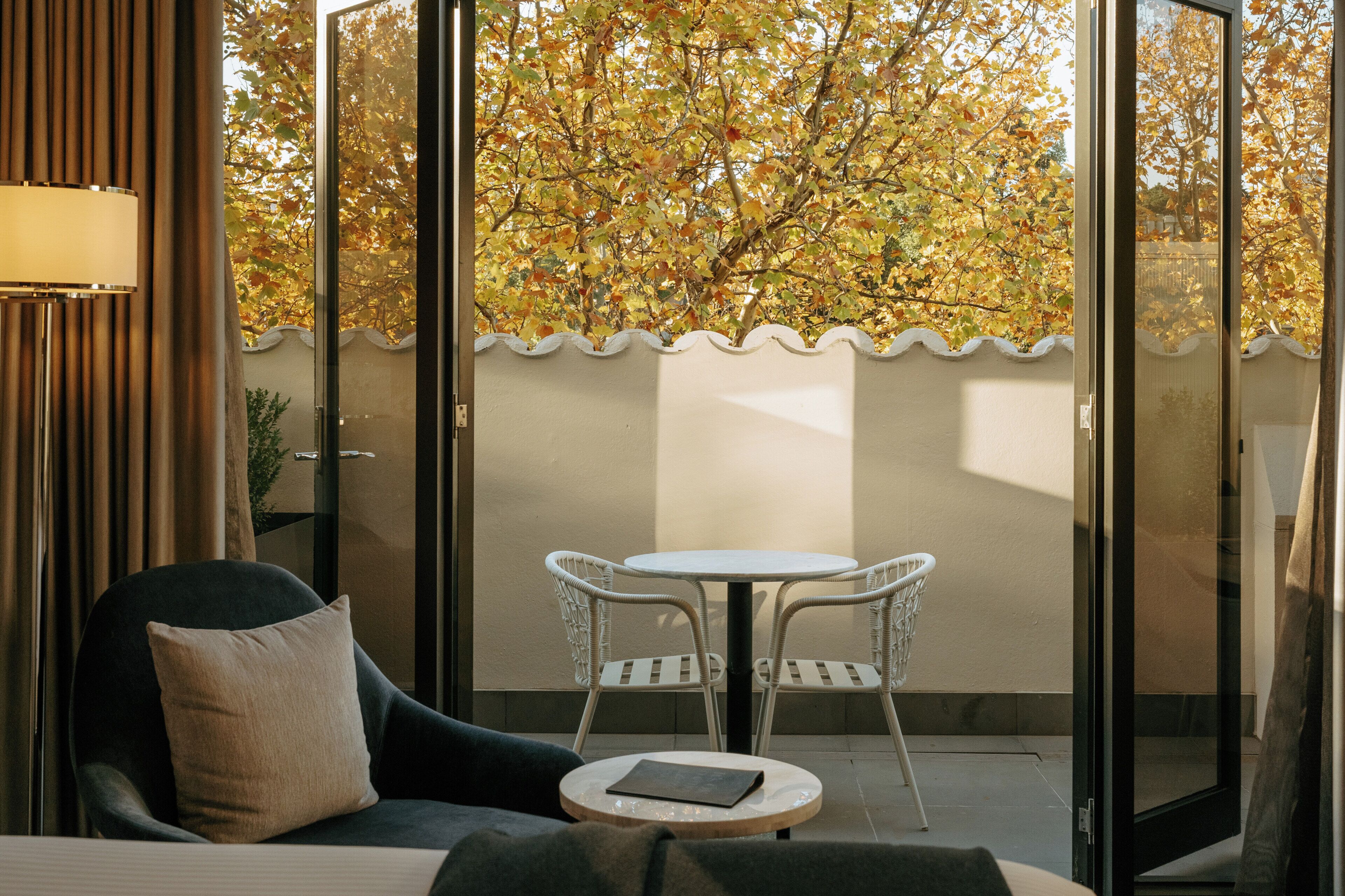 A room with a bed, a chair, a small table, and a view of trees through a glass door.